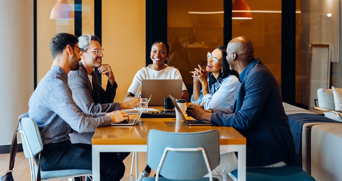 Five people sitting at a table using laptops